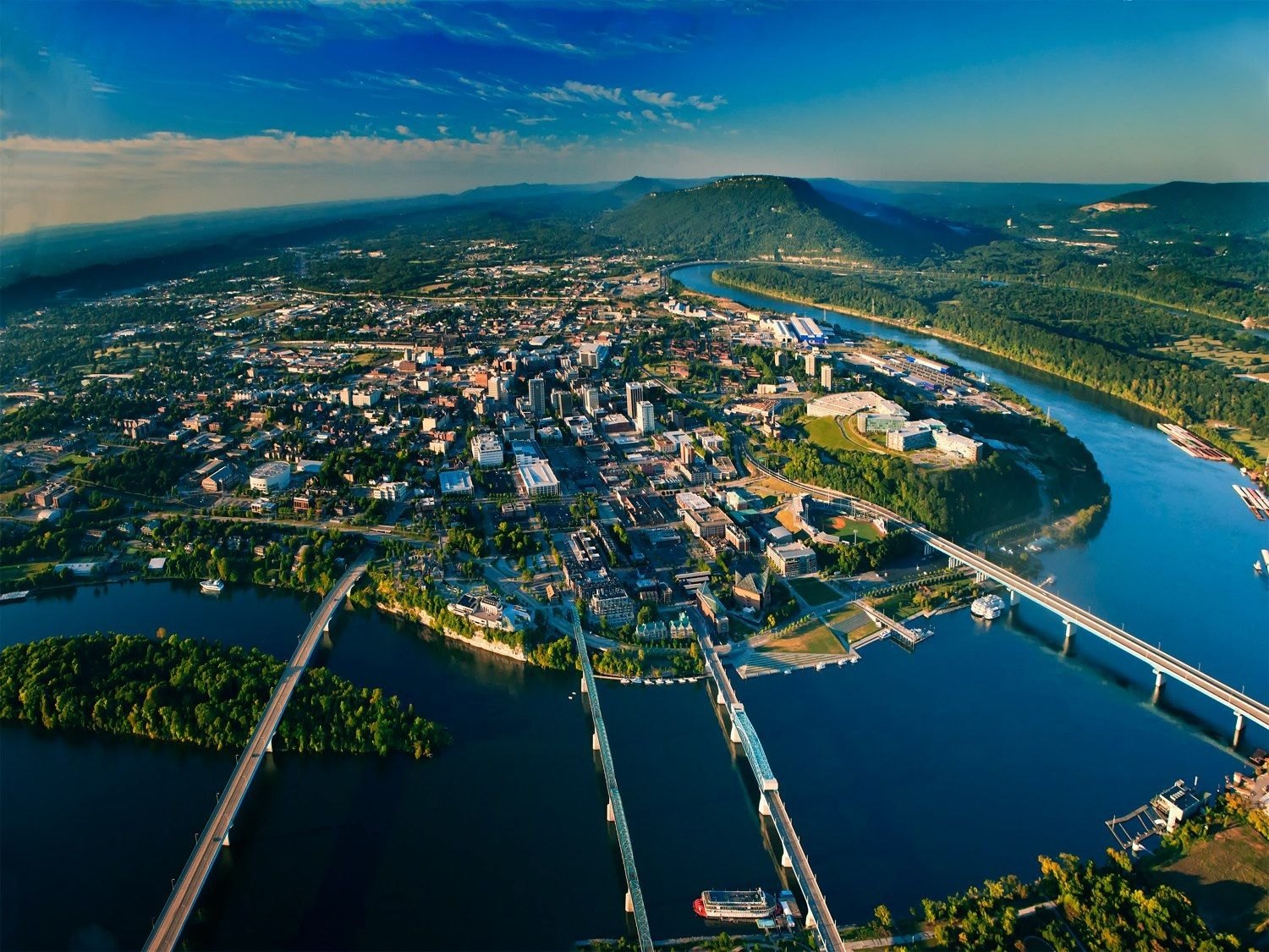 Aerial view of downtown Chattanooga at the bend of the Tennessee River, with the Walnut Street pedestrian bridge and Lookout Mountain in the distance.
