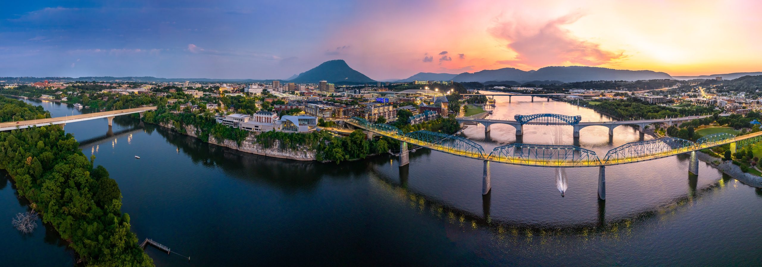 Aerial view of downtown Chattanooga with the Tennessee River, Walnut Street Bridge, and Lookout Mountain in the distance.