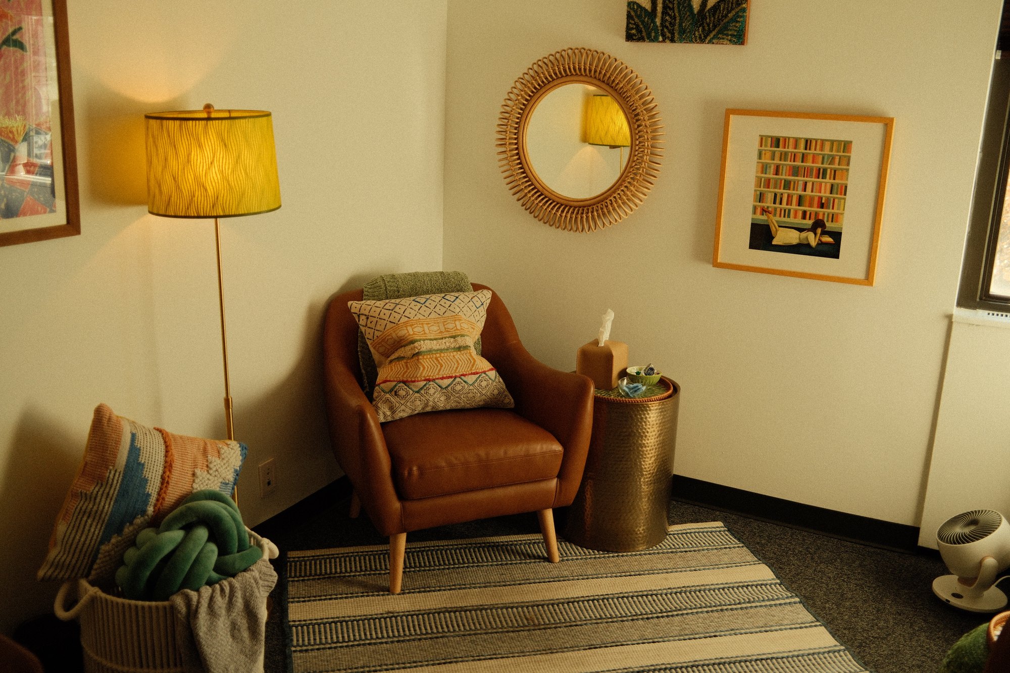 A reading corner with a leather chair, green knit ottoman, and abstract artwork.