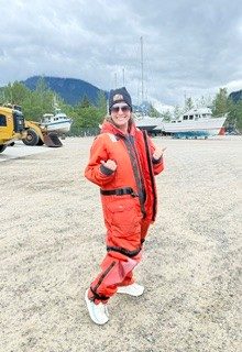Ann Hatcher giving a thumbs up in a survival suit on a boat dock in Alaska.