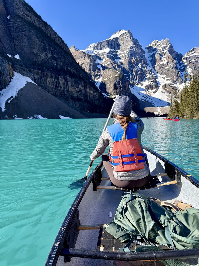 Cayce Smith canoeing on a turquoise lake surrounded by mountains.