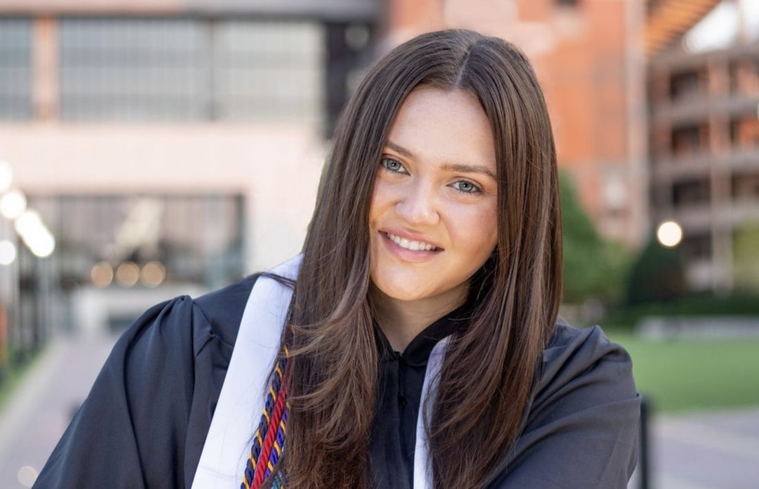 Elena Godbout smiling in her graduation cap and gown on a college campus.