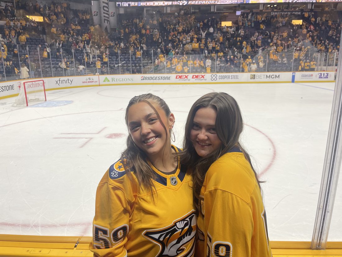 Elena Godbout with a friend at a Nashville Predators hockey game, wearing team jerseys.