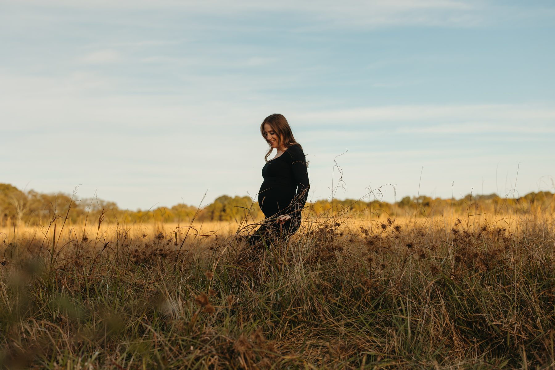 Jess Mansell, pregnant, walking through a golden field during a maternity photo session.