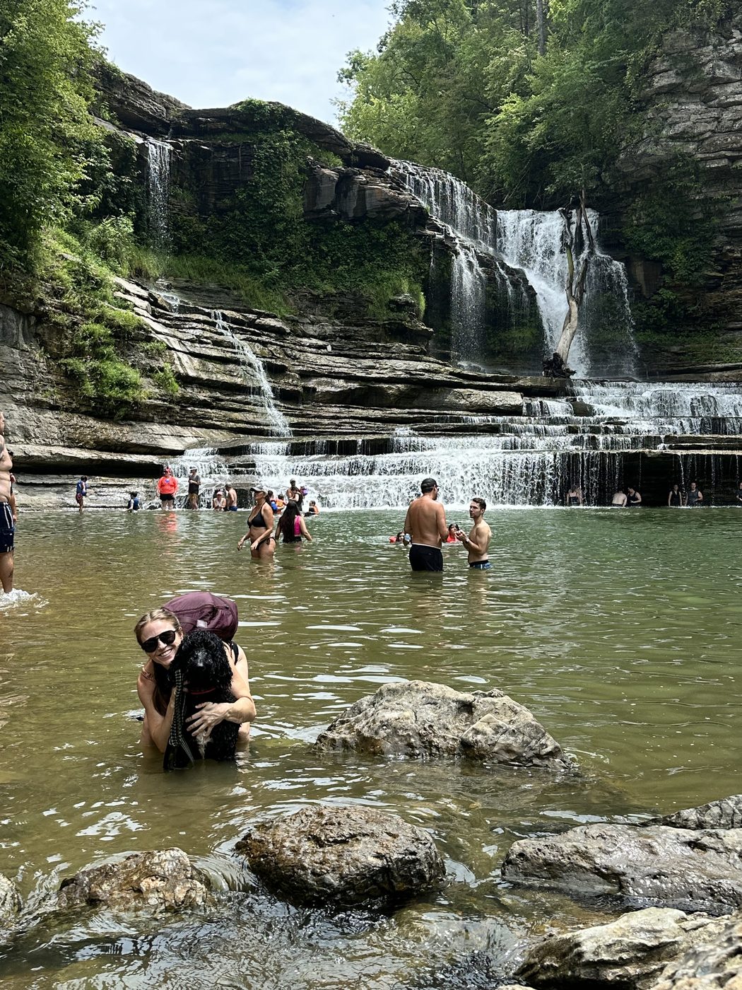 Jess Mansell smiling in the water with her dog in front of a waterfall.