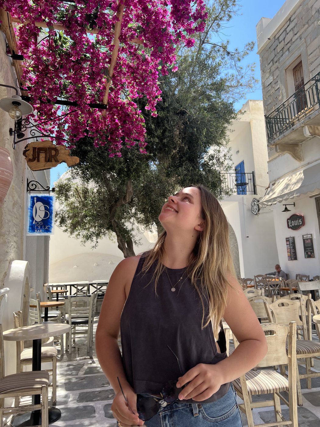 Jillee Walter smiling up at a bougainvillea tree in a Greek island courtyard cafe.