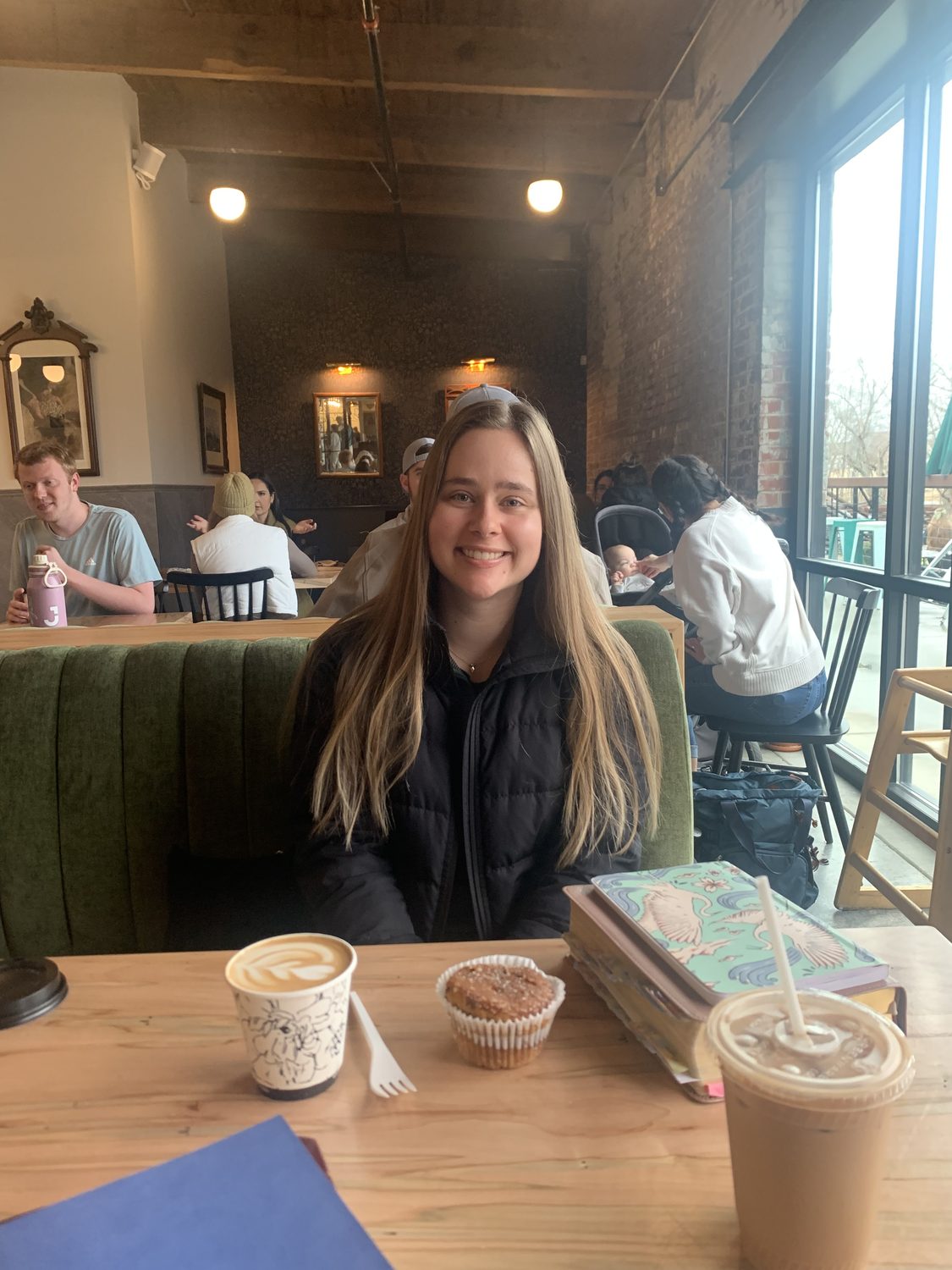 Jillee Walter smiling at a coffee shop table with a latte and pastry.
