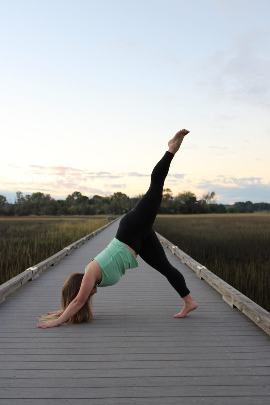 Jillee Walter practicing a yoga pose on a boardwalk over a marsh at sunset.